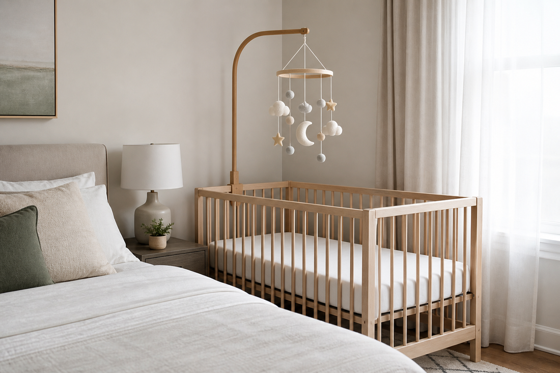 Soft modern parent bedroom nursery corner with a baby mobile mounted high above a bare crib beside the parents' bed in gentle daylight