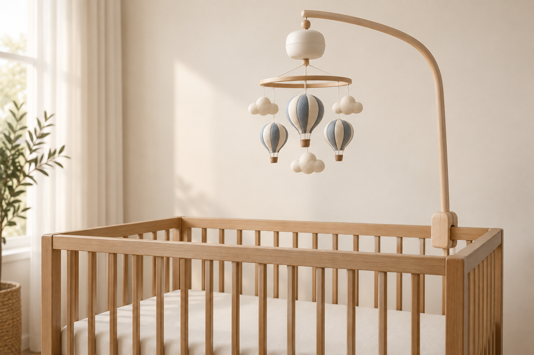 Blue and cream balloon mobile with an ivory music unit mounted high above a bare oak crib in soft daylight