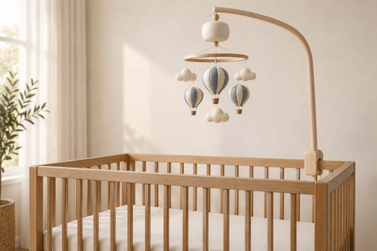 Blue and cream balloon mobile with an ivory music unit mounted high above a bare oak crib in soft daylight