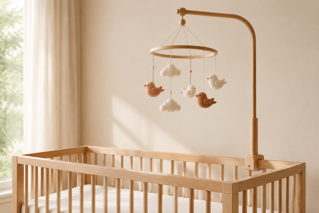 Cream and terracotta bird-and-cloud mobile on a wooden arm above an empty crib with a fitted sheet