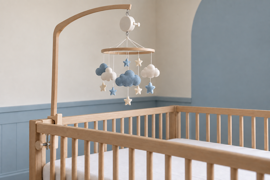 Blue and ivory cloud mobile with a wind-up music box on a wooden arm above a bare oak crib
