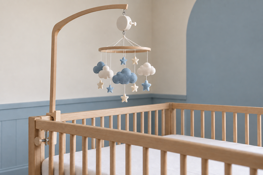 Blue and ivory cloud mobile with a wind-up music box on a wooden arm above a bare oak crib